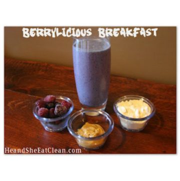blueberry protein shake in a glass on a wooden table with berries, peanut butter, and protein powder