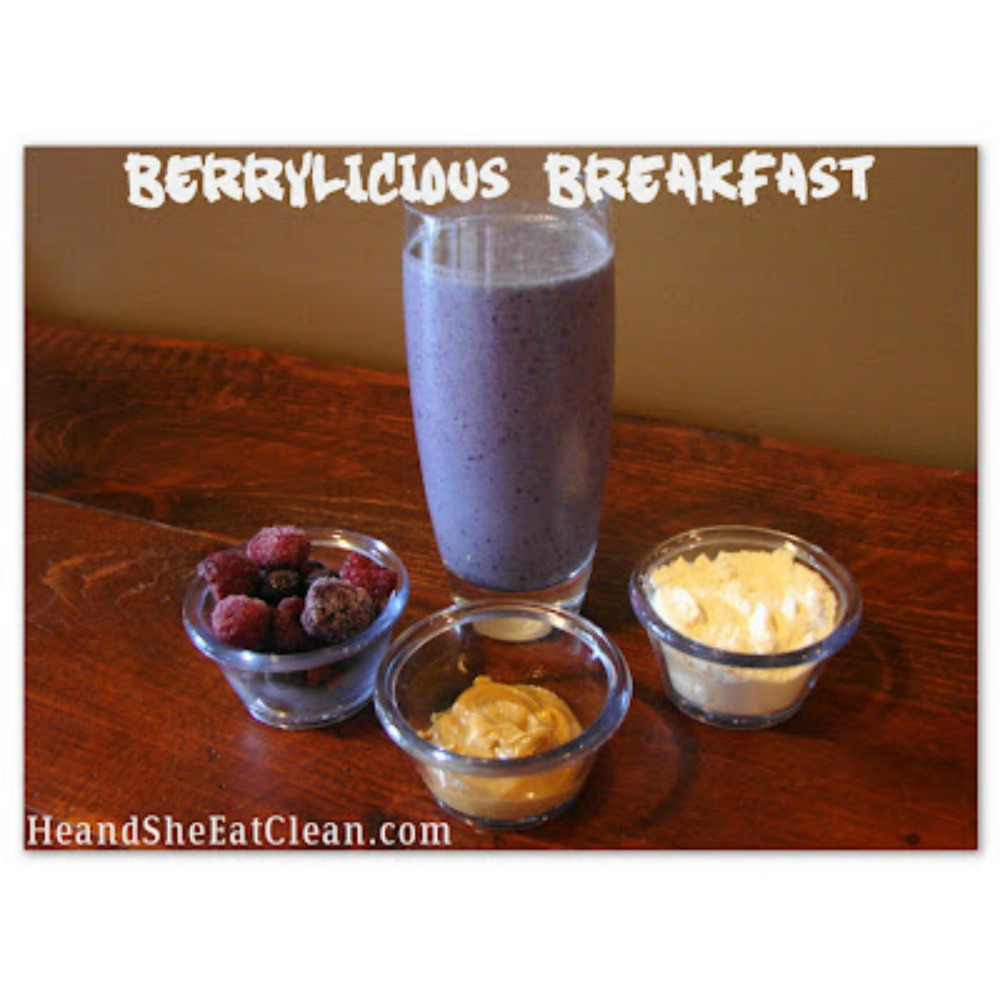 blueberry protein shake in a glass on a wooden table with berries, peanut butter, and protein powder