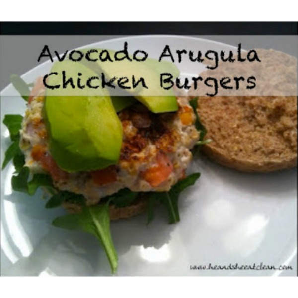 chicken burger with avocado and arugula on top on a white plate
