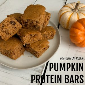 stack of pumpkin protein bars on a white plate with 2 small pumpkins behind the plate square image