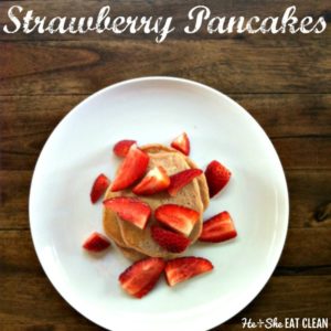 stacked pancakes topped with strawberries on a white place