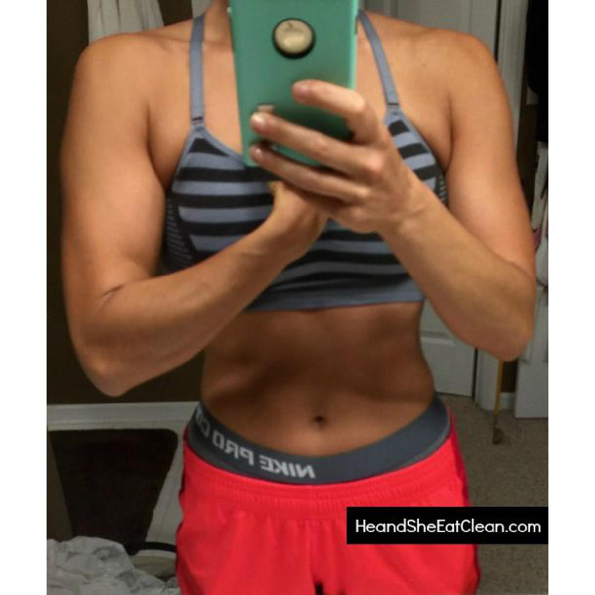 female taking a selfie flexing in a mirror wearing sports bra and pink shorts