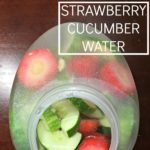 jug filled with water and strawberries and cucumbers on a wooden table