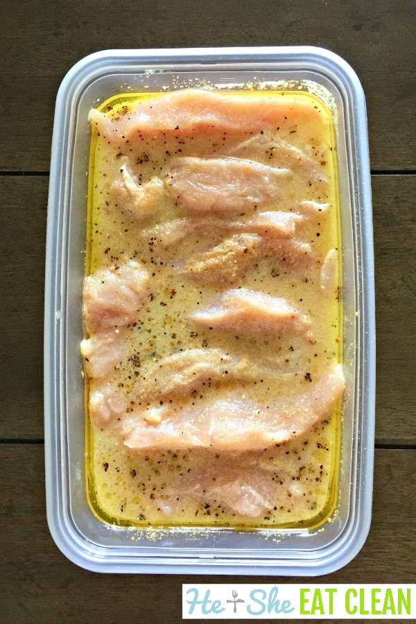 raw chicken breasts marinating in orange juice and seasonings in a plastic container