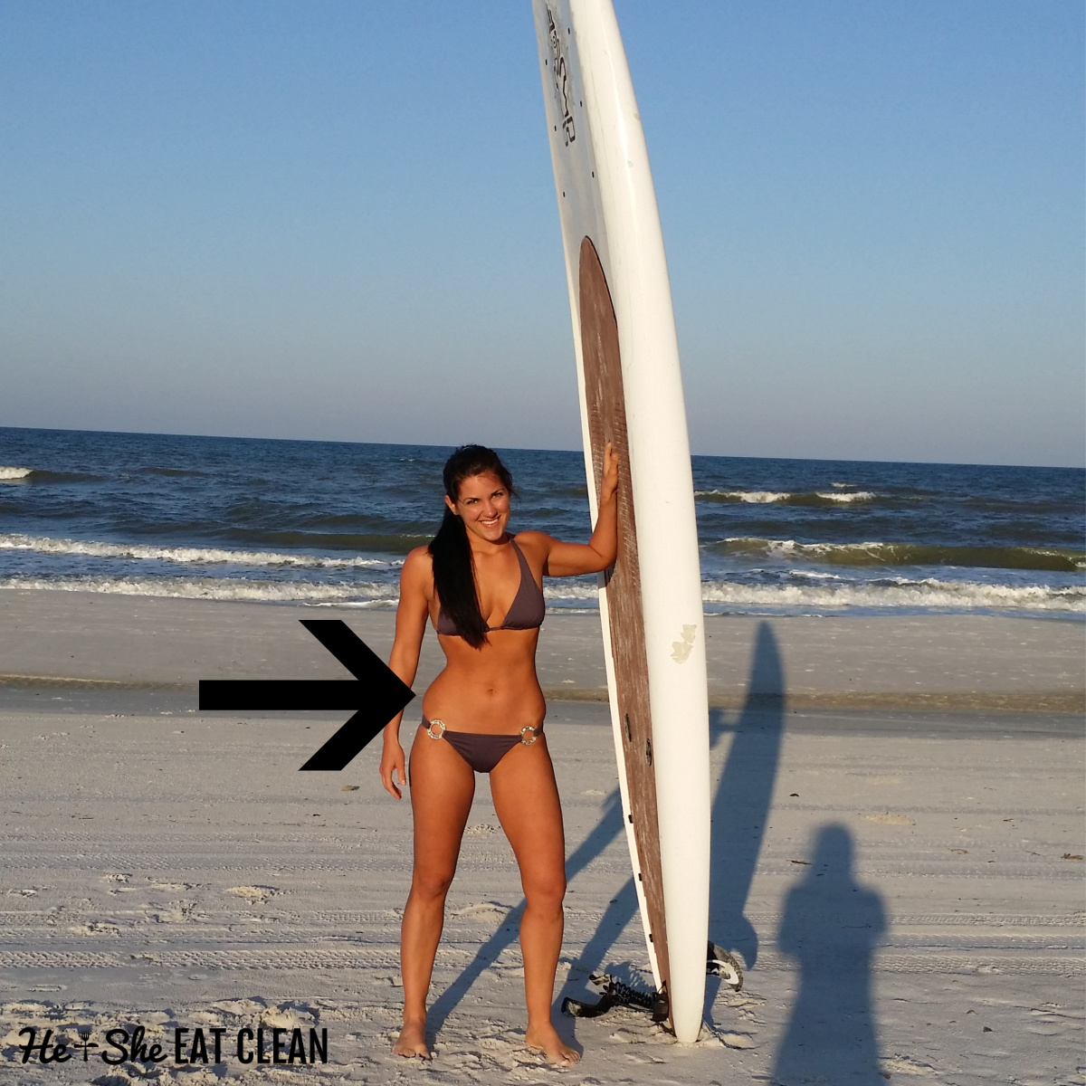 square image female standing next to a paddleboard in a purple bikini