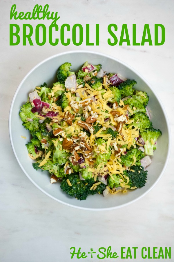 broccoli salad topped with cheddar cheese and pecans in a white bowl on a white marble top