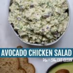 bowl of avocado chicken salad with toast and avocado below on a white marble slab