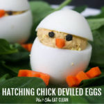 deviled egg made to look like a chick with carrot feet and peppercorn eyes on a bed of spinach with another one in the background