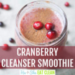 cranberry smoothie in a mason jar with cinnamon and fresh cranberries on top and cranberries scatter around the mason jar